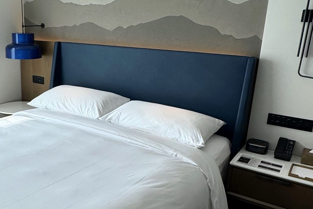 シェラトン鹿児島のキングベッド。紺のヘッドボードと山並みの壁画、左右のナイトテーブルに電源パネルとスイッチ
