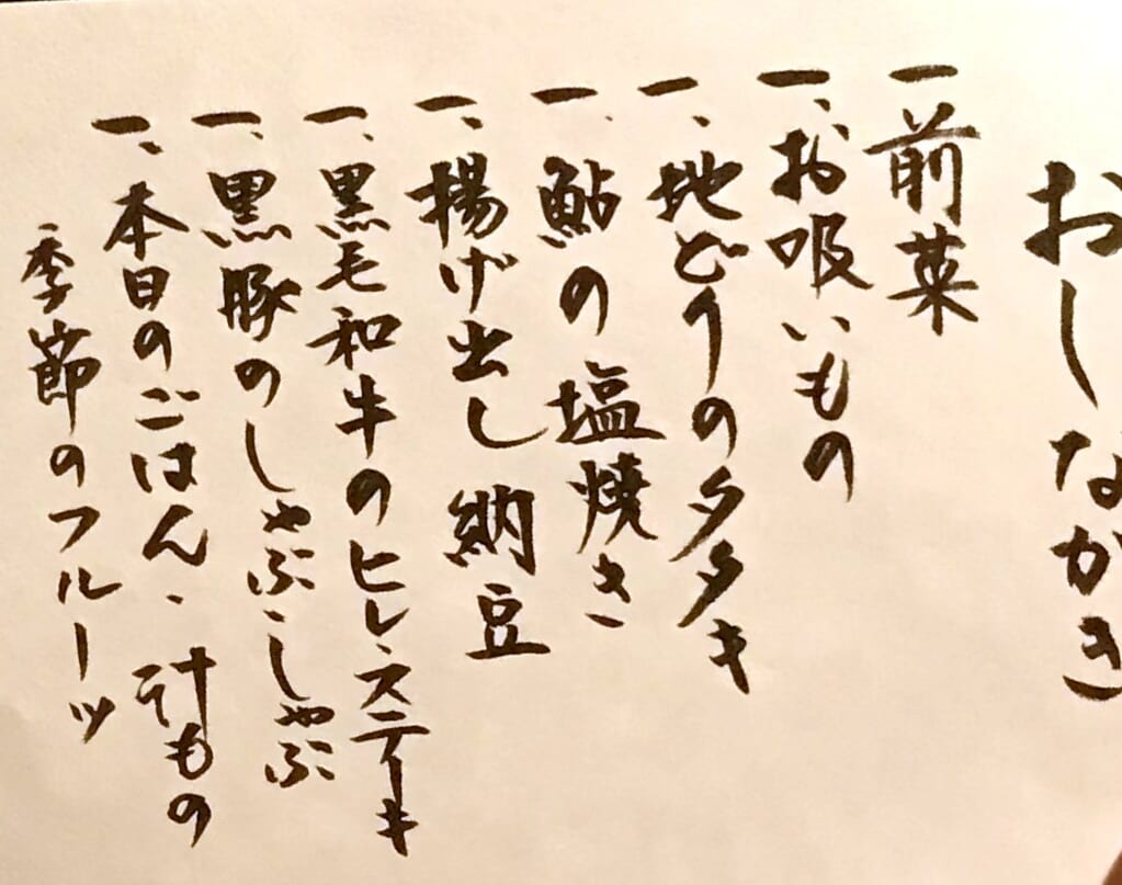 摘み草の宿こまつの手書きのおしながき。前菜、お吸いもの、地鶏のタタキ、鮎の塩焼き、揚げ出し納豆、黒毛和牛のヒレステーキ、黒豚のしゃぶしゃぶ、ごはんと汁もの、季節のフルーツ
