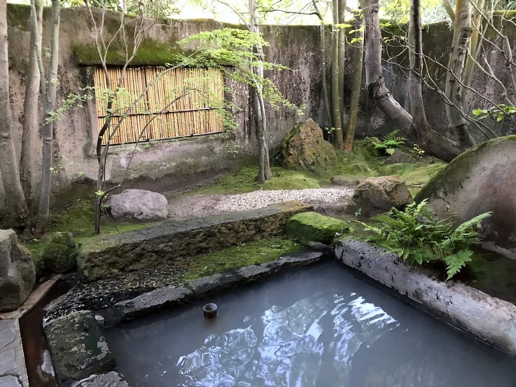 摘み草の宿こまつの客室露天風呂。苔庭を土塀が囲み、湯は白く濁っている